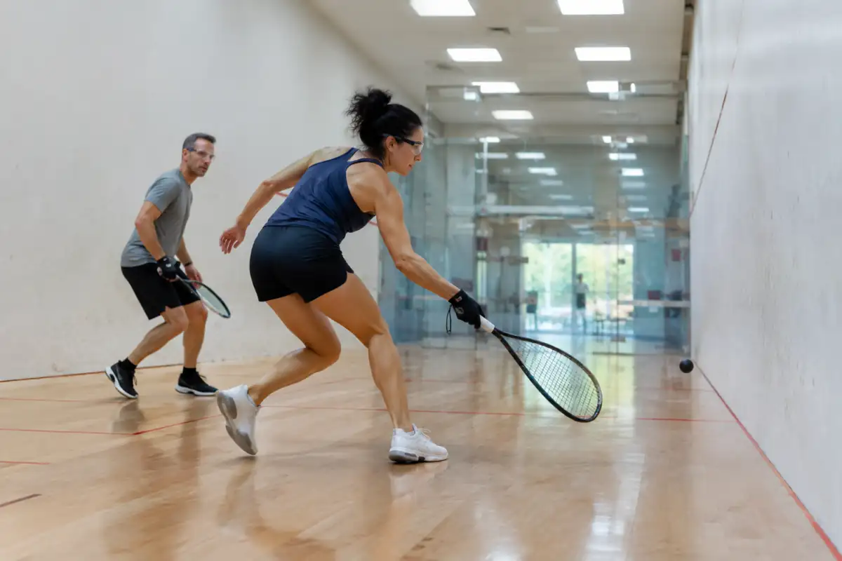 Échange de racquetball dans un court fermé : un joueur frappe la balle avec lunettes de protection et raquette courte.
