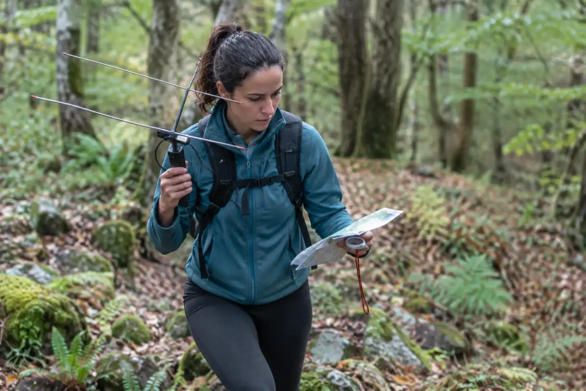 Un participant en radio-orientation suit une carte et une antenne directionnelle dans une forêt.