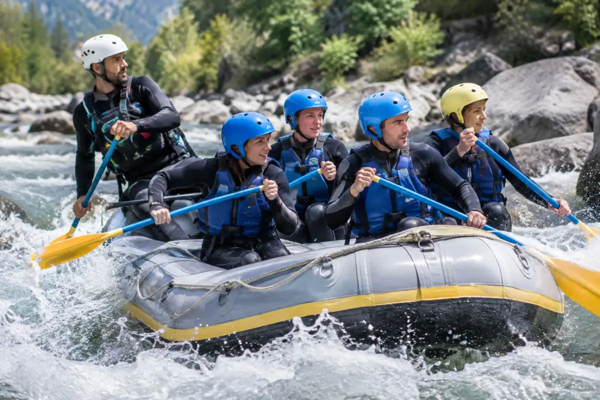 Équipage en rafting pagayant dans un rapide alpin, équipé de casques, gilets et combinaisons néoprène.