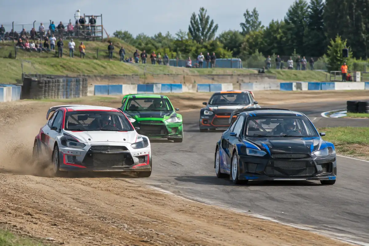 Voitures de rallycross en peloton dans un virage, entre terre et asphalte, sur un circuit français.