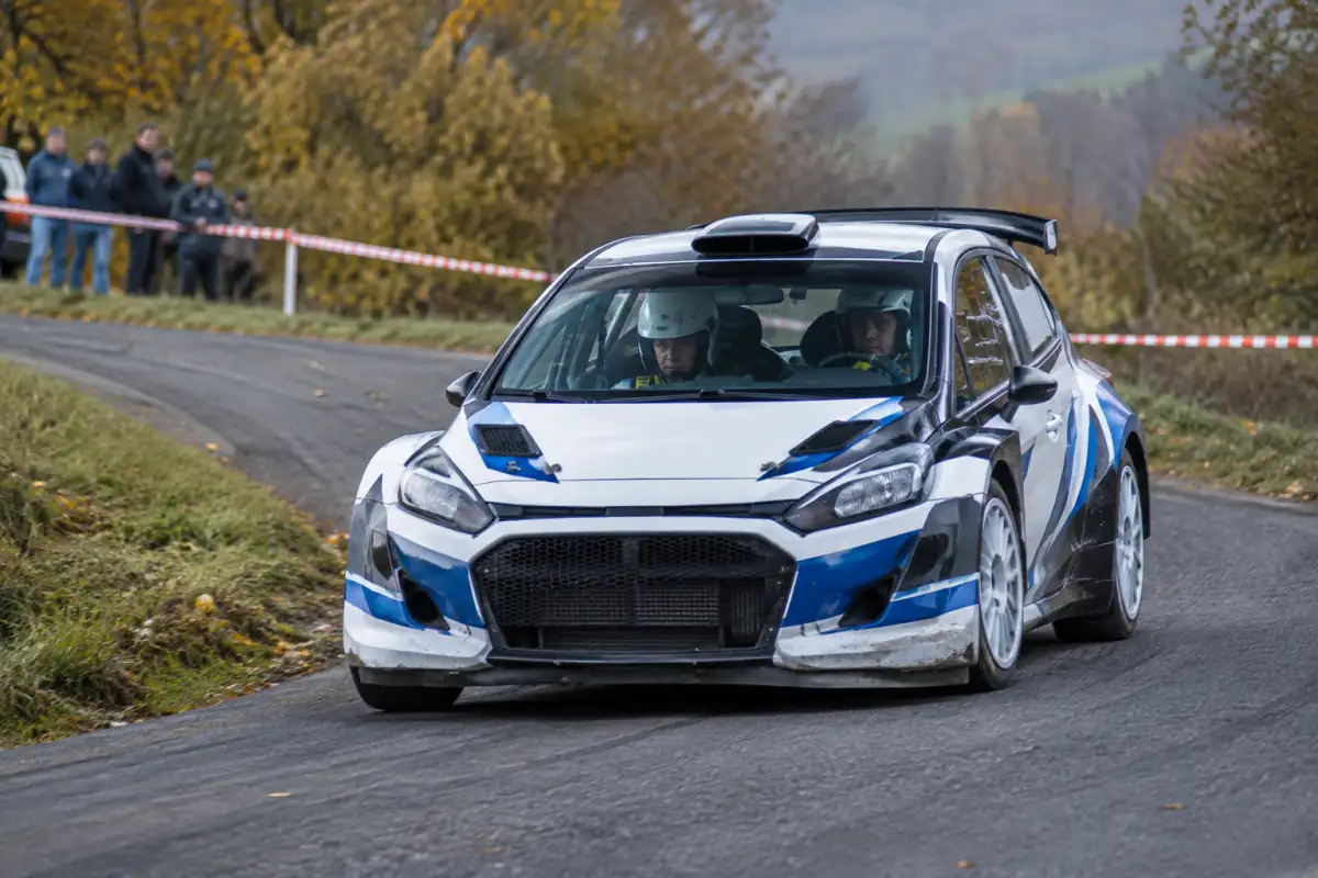Une voiture de rallye et son équipage négocient un virage sur une spéciale fermée en campagne française.