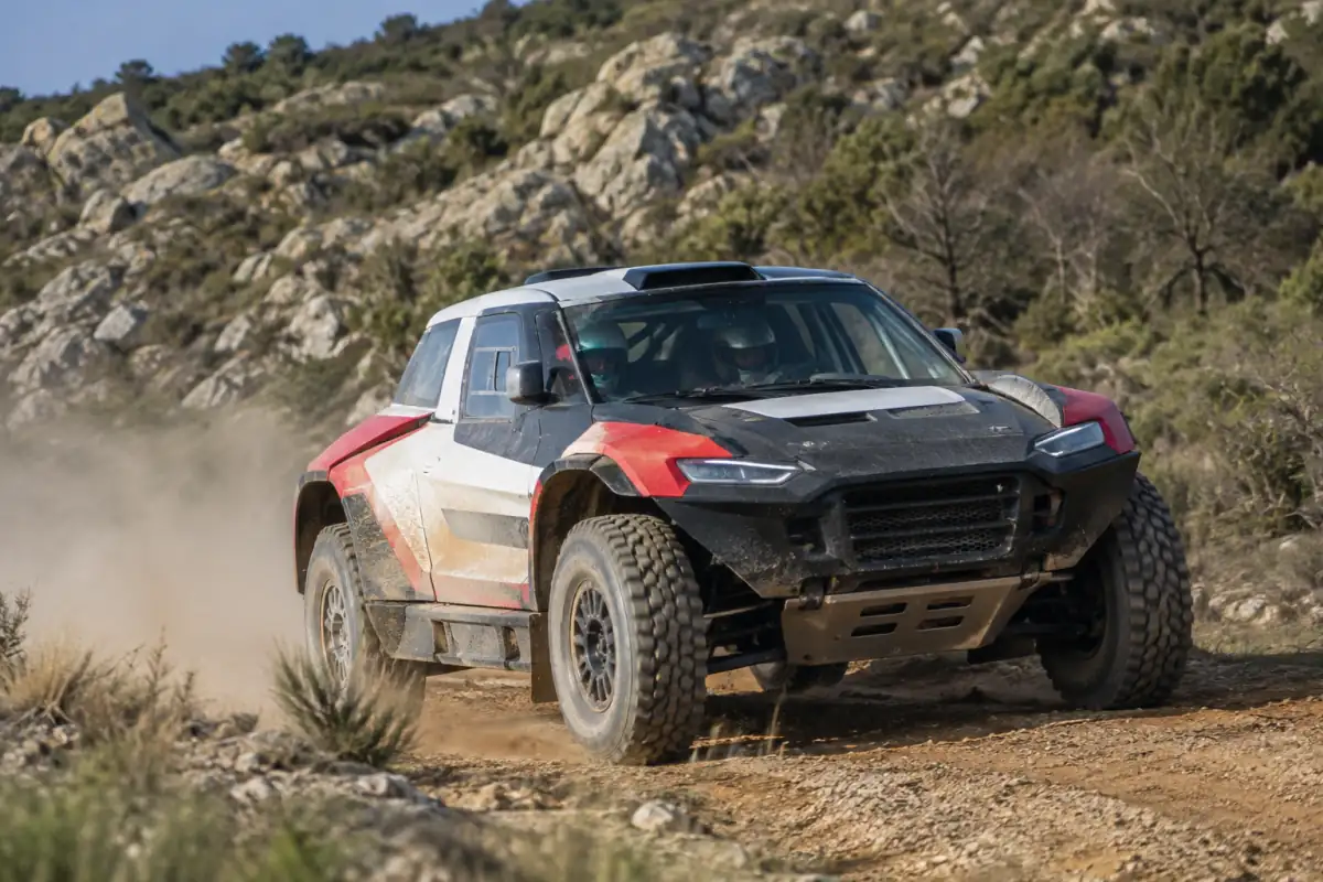 Voiture de rallye-raid automobile préparée en virage sur une piste poussiéreuse, avec pilote et copilote équipés de casques.