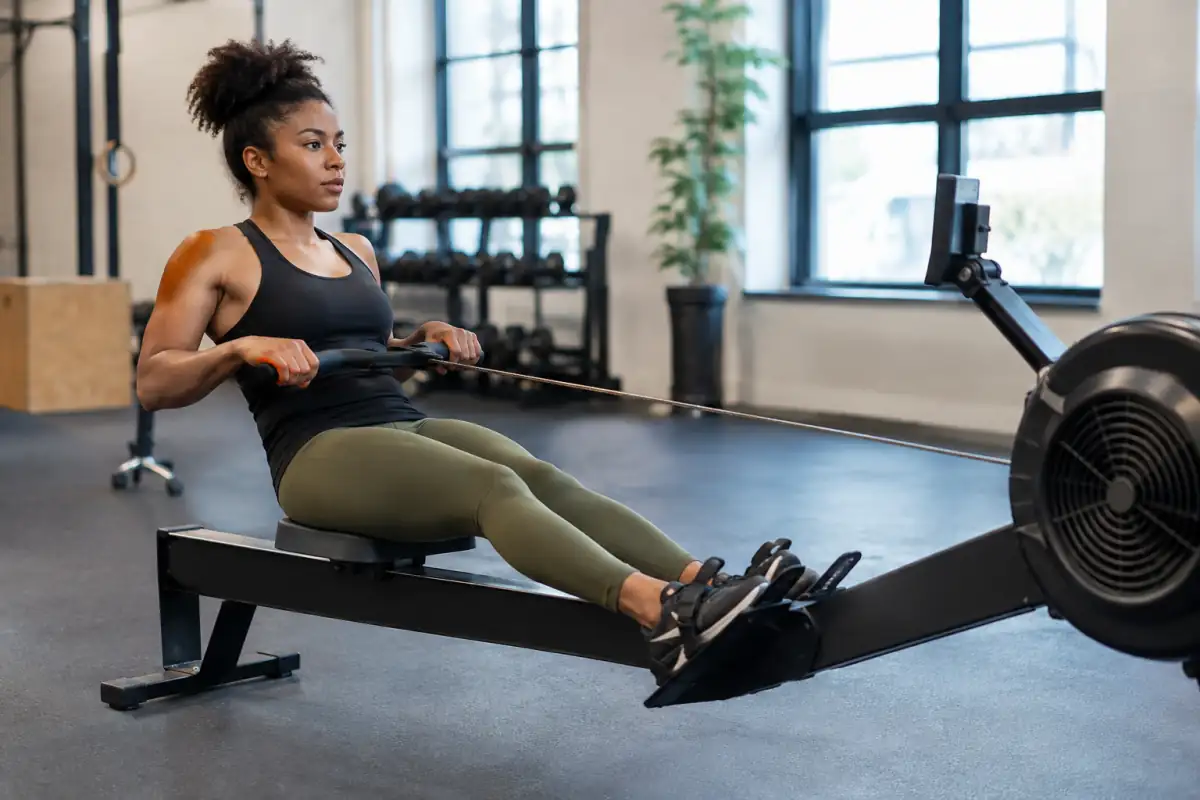 Pratiquante de rameur indoor en salle, poussant sur les jambes et tirant la poignée vers le bas des côtes.