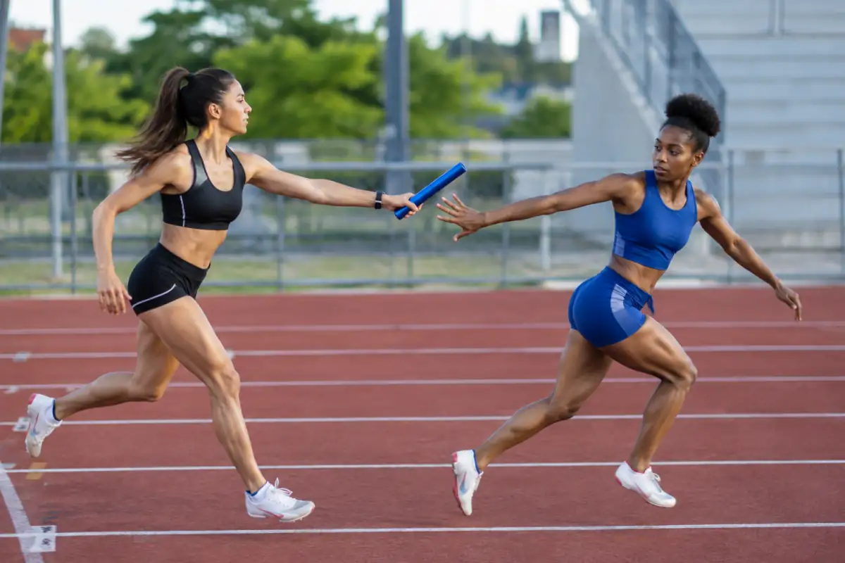 Passage de témoin en relais 4 × 100 m dans une zone balisée, avec les deux athlètes courant dans leur couloir.