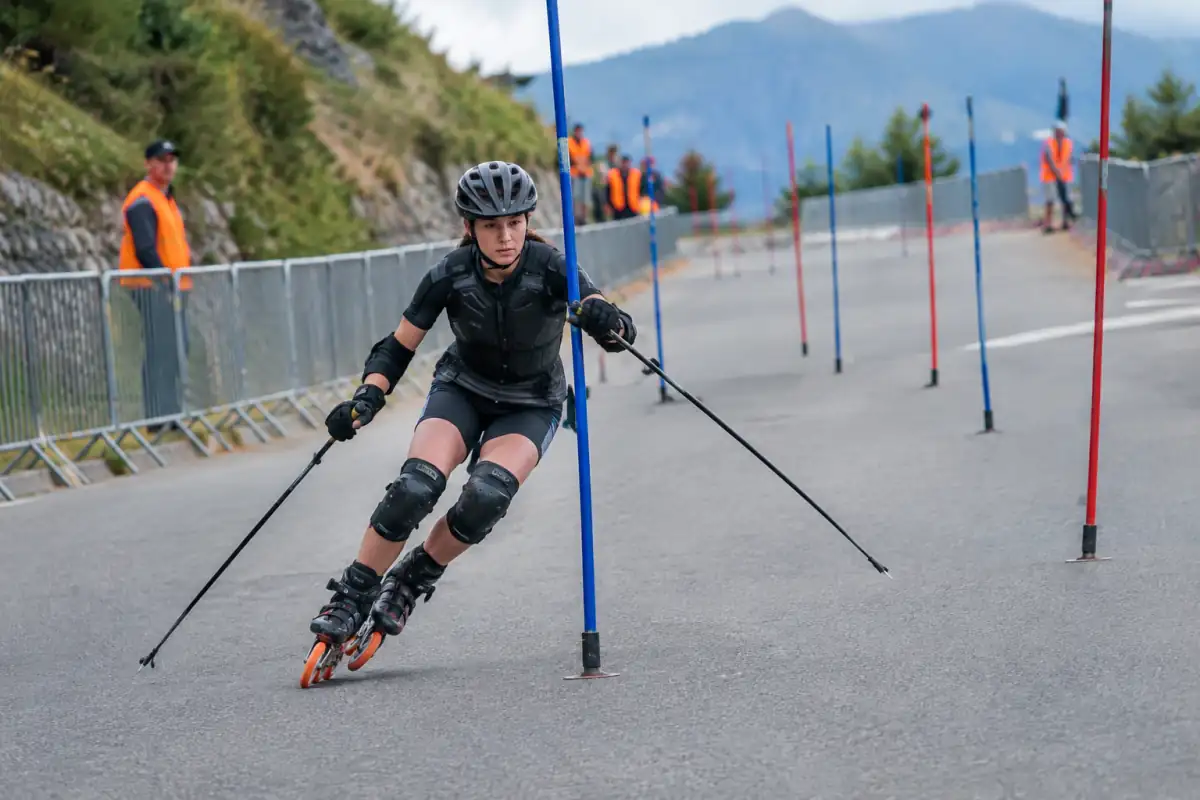 Patineur en roller alpin franchissant une porte sur une route fermée, casque et protections portés pendant une descente.