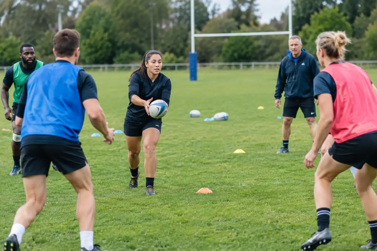 Débutants au rugby à XV testant la passe et le placement sur un terrain, sous les conseils d’un entraîneur.