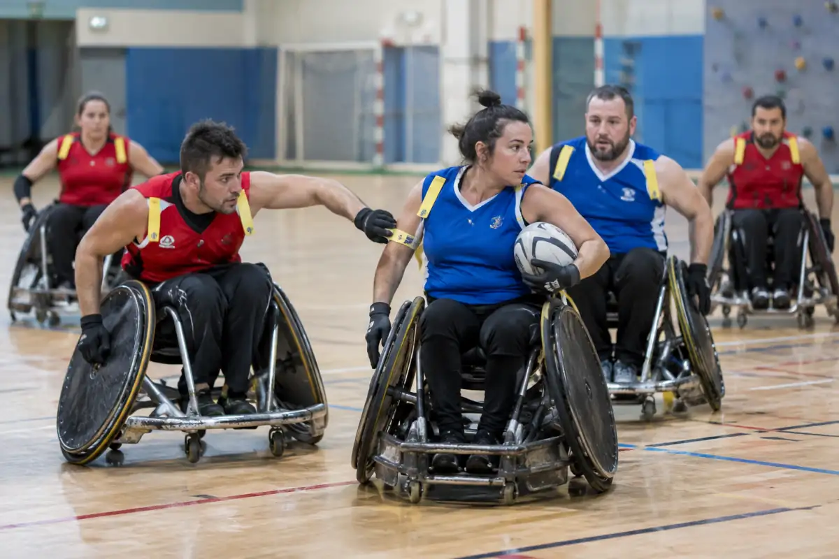 Un joueur porte le ballon ovale en fauteuil tandis qu’un adversaire tente de retirer son tag lors d’un match de rugby fauteuil à XIII.