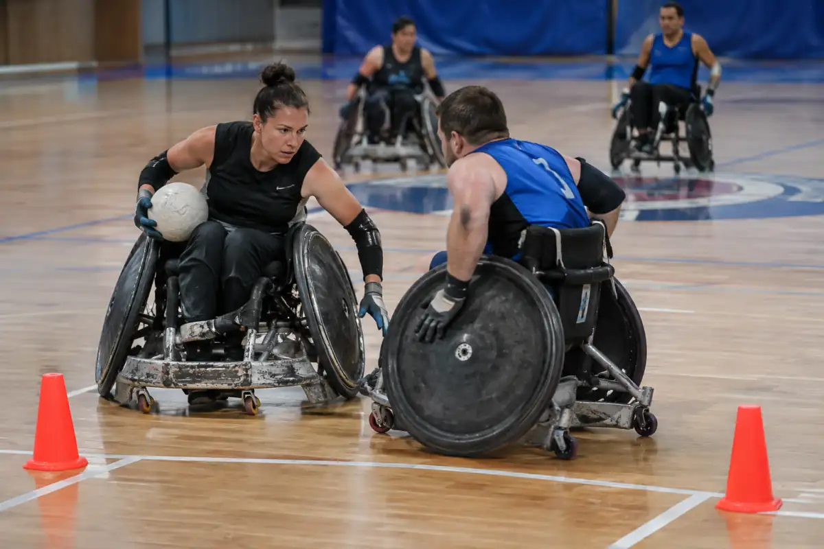 Action de rugby fauteuil près de la ligne de but, avec un joueur en possession du ballon et un défenseur en fauteuil face à la porte.