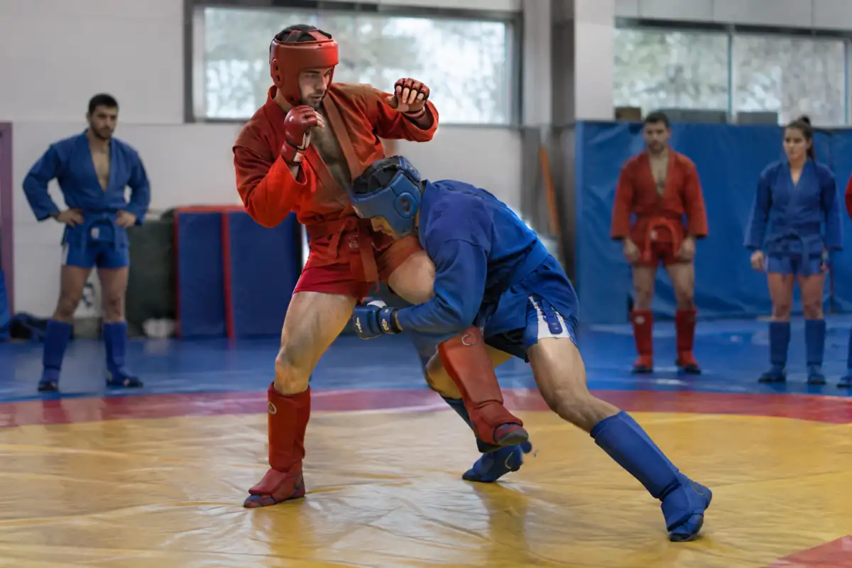 Deux pratiquants de sambo de combat en tenue et protections travaillent une projection sur le tapis d’une salle.