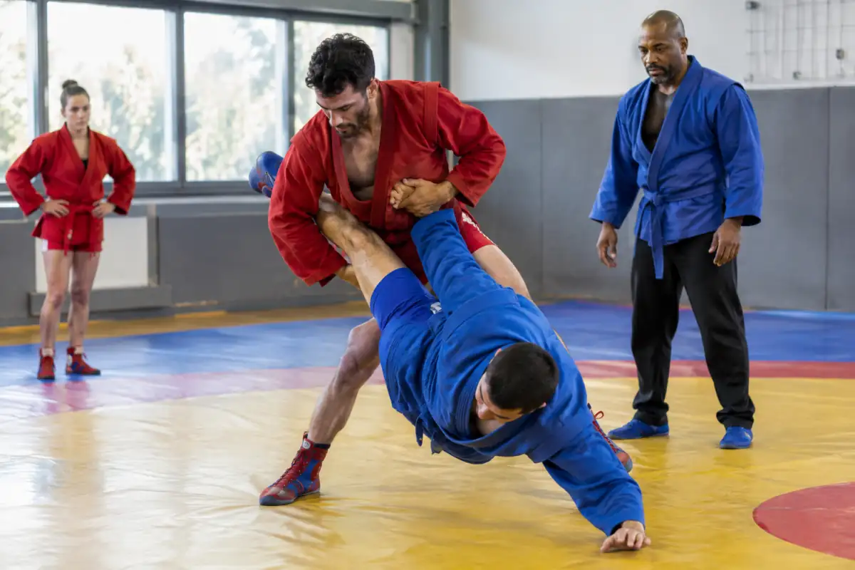 Deux samboïstes en kourka rouge et bleue travaillent une projection sur le tapis lors d’un entraînement encadré.