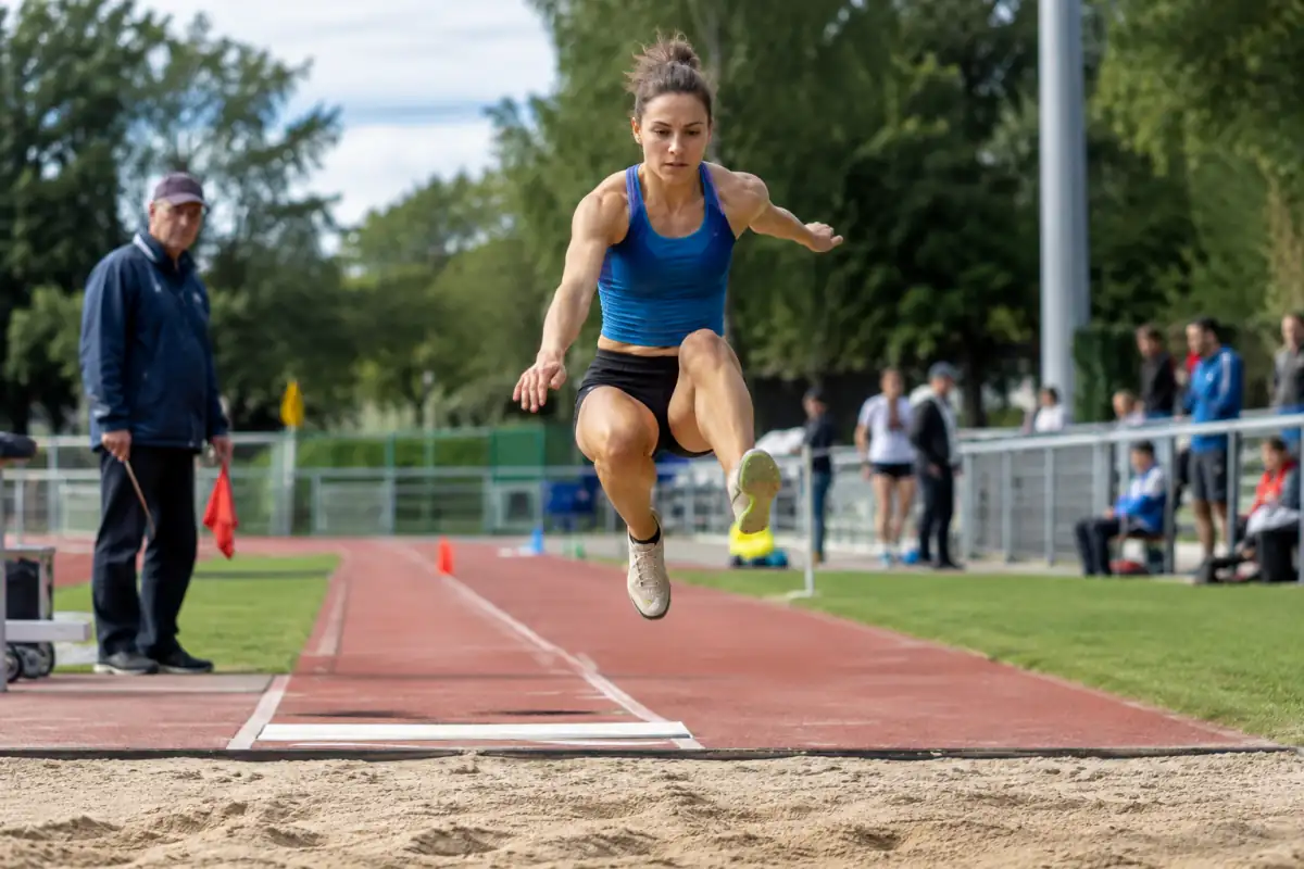 Un athlète en plein saut en longueur au-dessus du bac à sable, après son appel sur une piste d’athlétisme.