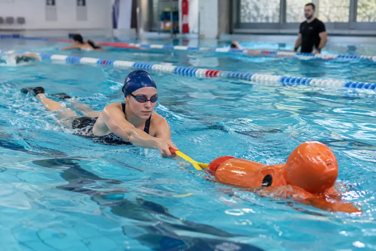 Athlète en palmes remorquant un mannequin avec une bouée tube lors d’un entraînement de sauvetage sportif en piscine.