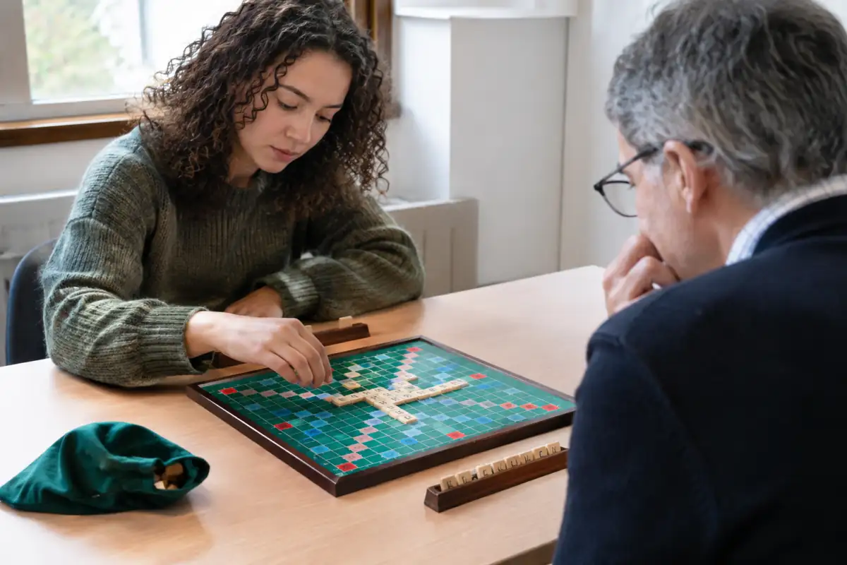 Deux joueurs concentrés posent des lettres sur le plateau lors d’une partie de Scrabble classique en club.