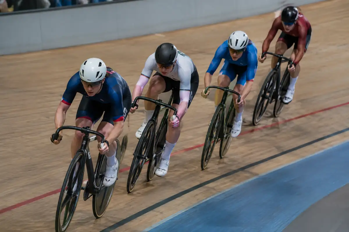 Course de scratch sur piste : des cyclistes en peloton accélèrent dans le virage incliné d’un vélodrome.