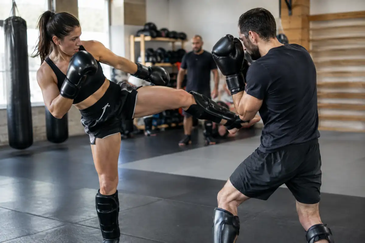 Deux pratiquants de shoot boxing s’entraînent en salle, l’un lançant un coup de pied tandis que l’autre garde sa posture.