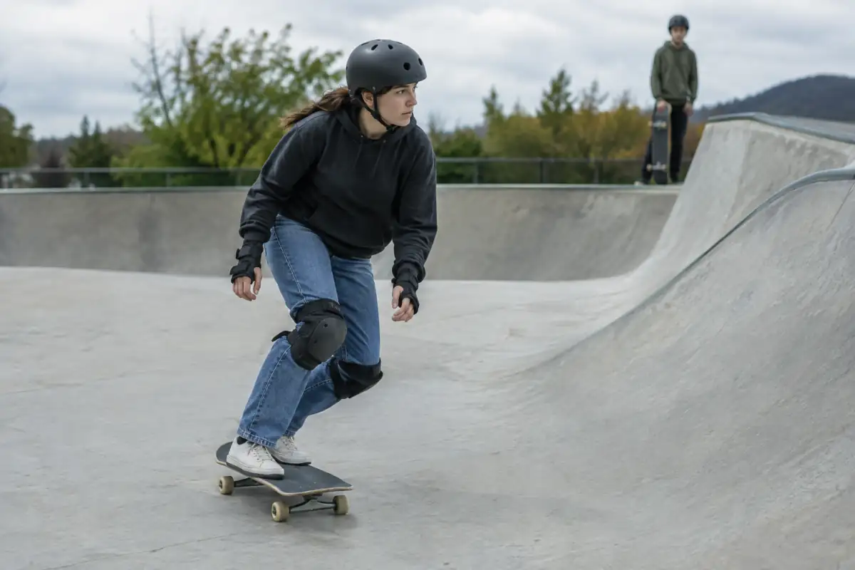 Un skateboarder travaille une trajectoire contrôlée dans un skatepark dégagé, avec un autre pratiquant en attente hors de la ligne.