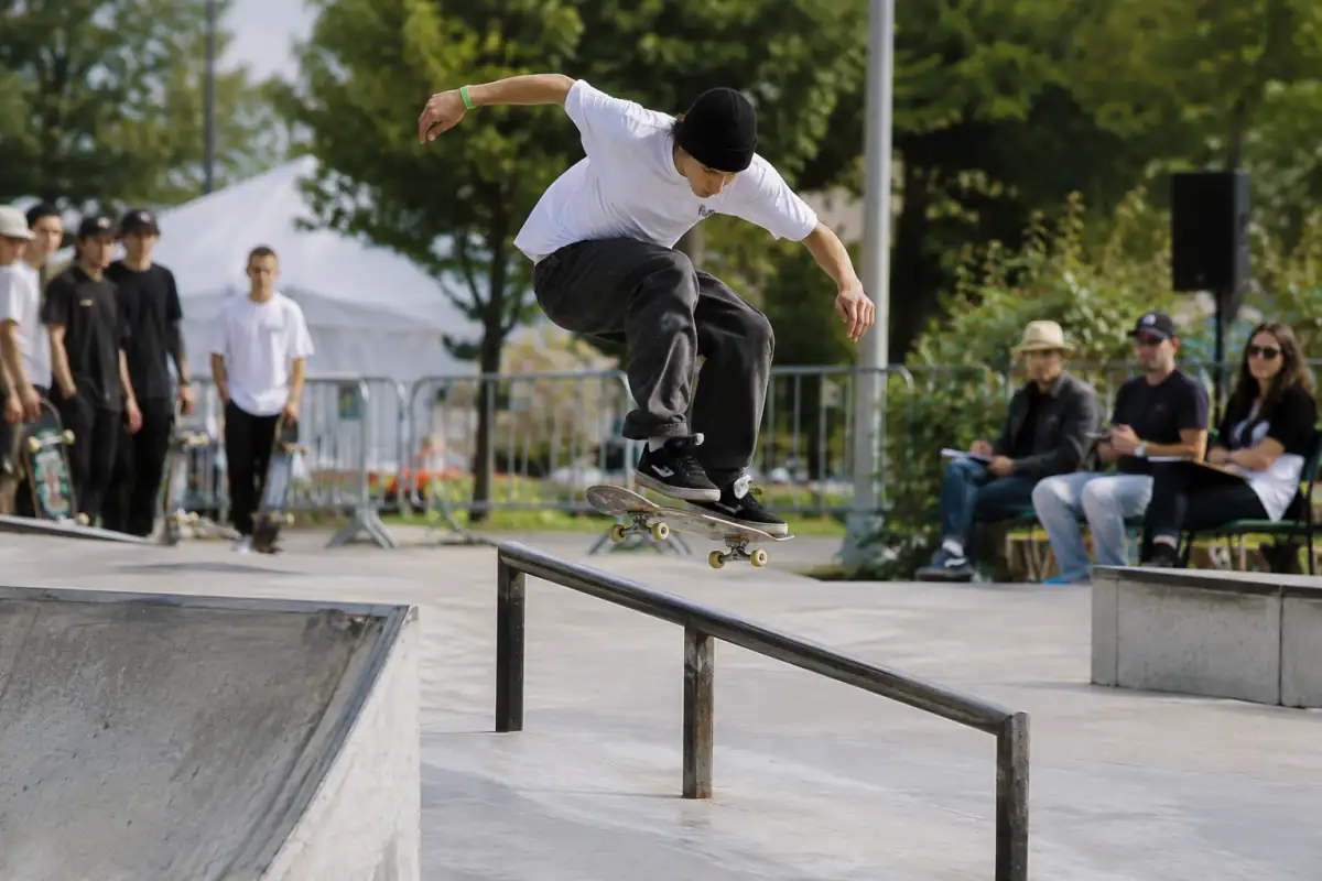 Un skateboardeur tente une figure sur un rail pendant une compétition de street, sous le regard du jury.