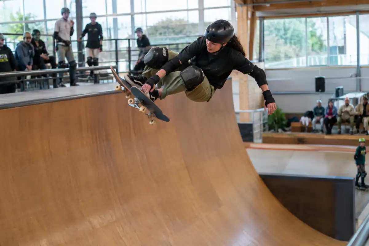 Skateur équipé de protections effectuant une figure aérienne au-dessus du coping d’une rampe de skateboard vert.