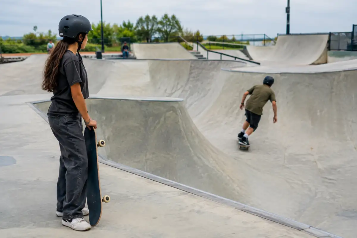 Un skateur attend hors de la trajectoire pendant qu’un autre termine sa ligne dans un bowl, avec les zones de passage dégagées.