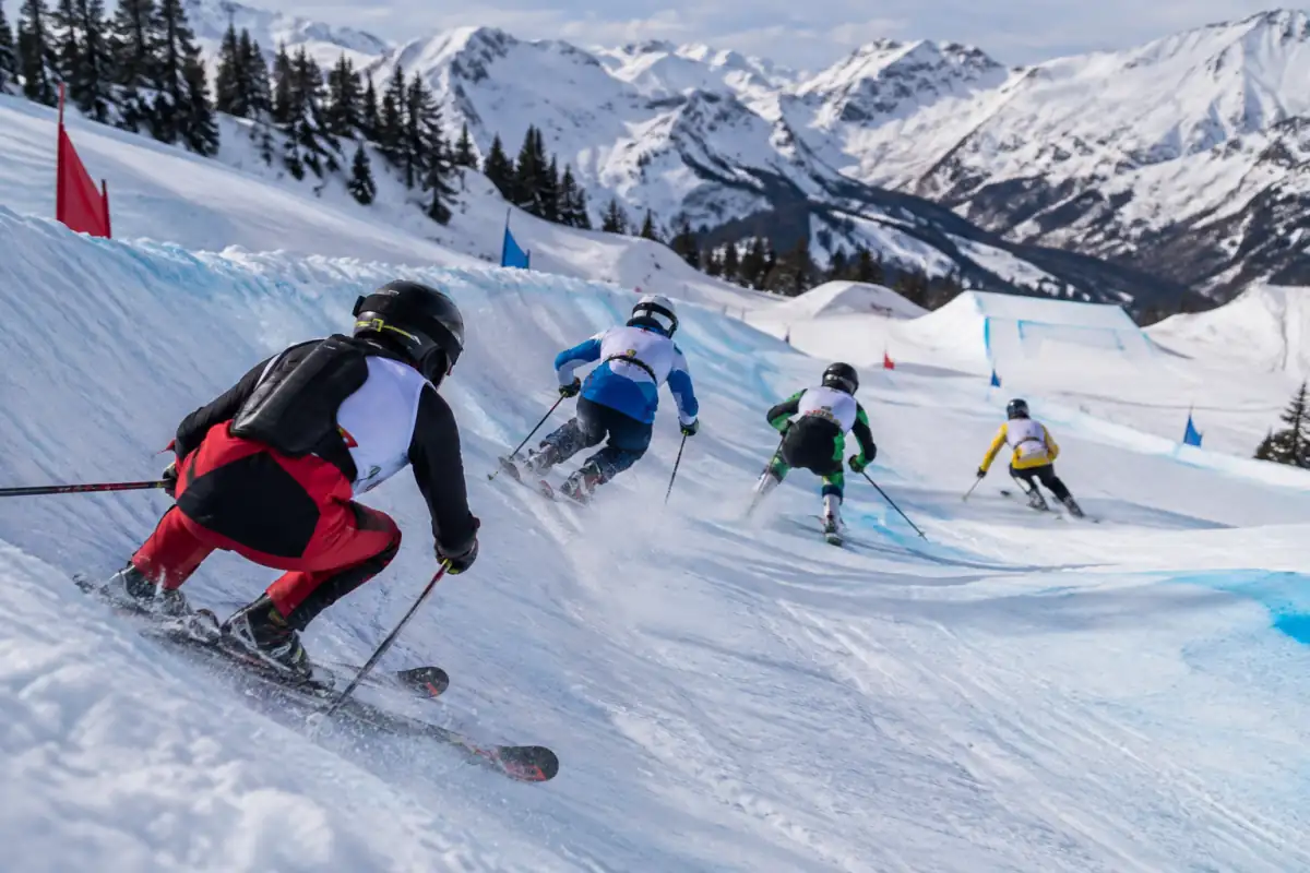 Quatre skieurs en casque négocient un virage relevé sur un parcours de ski cross enneigé en station.