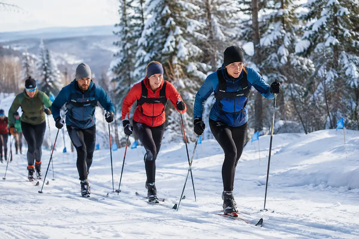 Groupe de fondeurs en départ groupé classique, skis dans les traces et bâtons plantés sur une montée enneigée.