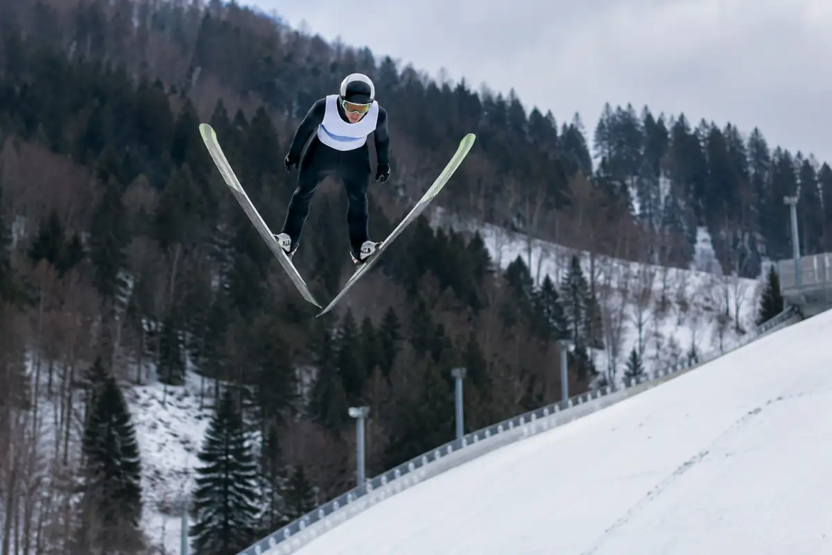 Sauteur en pleine position en V au-dessus d’un grand tremplin de ski volant enneigé, avec casque et combinaison de compétition.