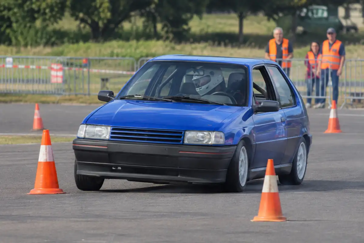 Une voiture compacte négocie une porte de cônes sur un parcours fermé de slalom automobile, sous le regard des commissaires.