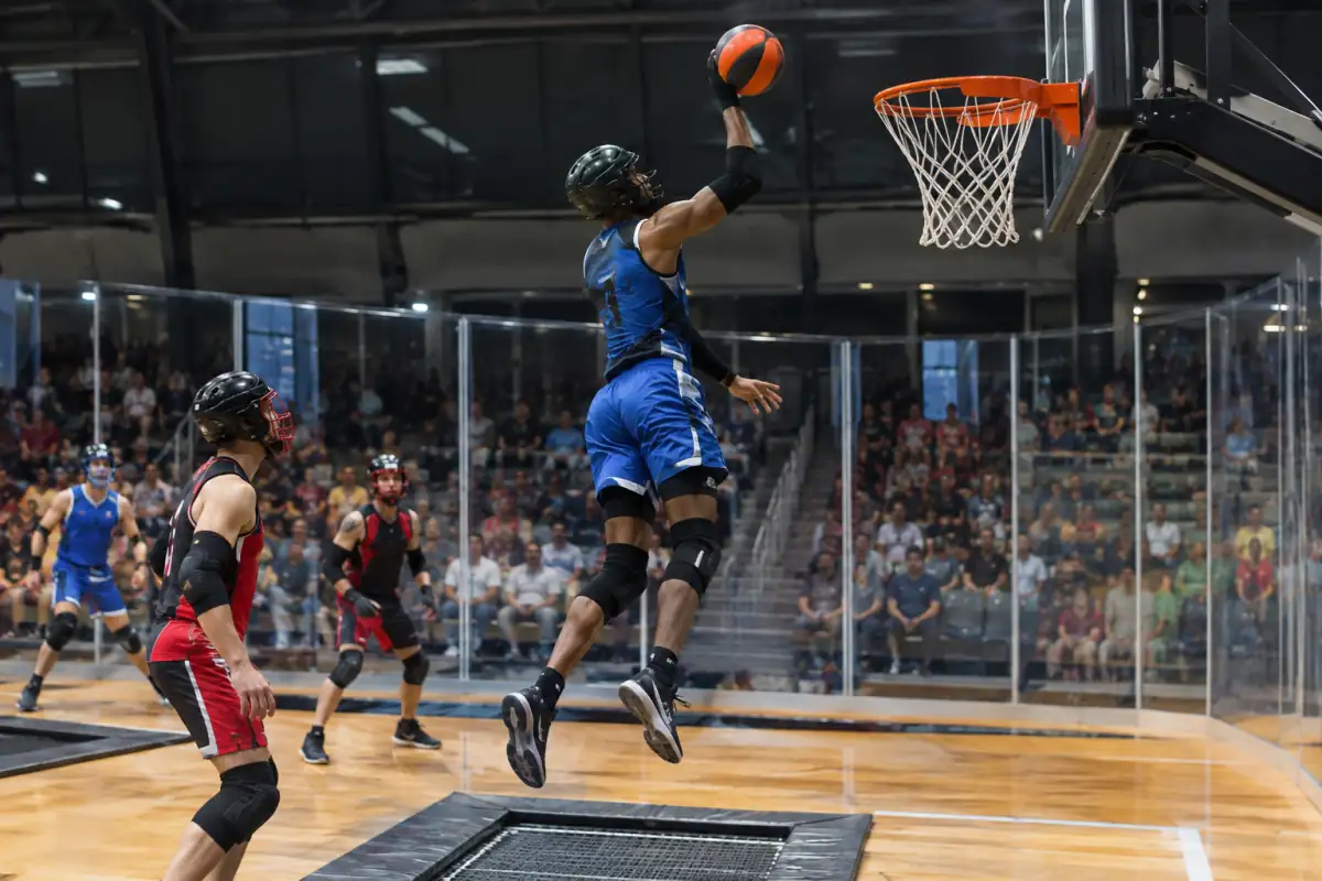 Un joueur casqué s’élève depuis un trampoline encastré pour marquer au panier pendant un match de Slamball en salle.