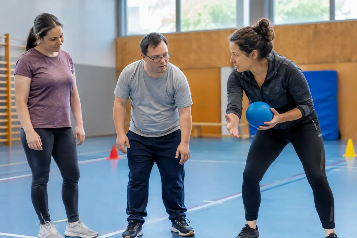 Un encadrant montre un exercice avec un ballon à un adulte débutant lors d’une séance d’essai de sport adapté.