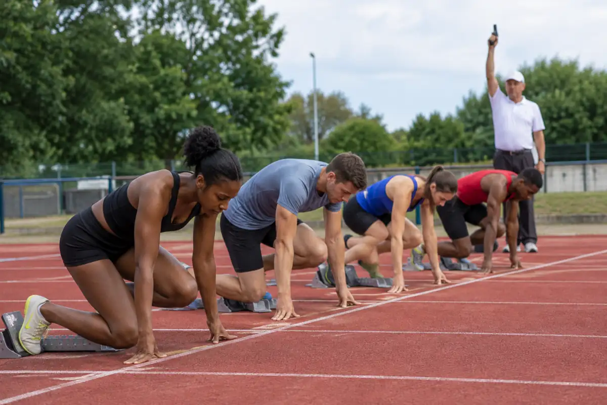 Sprinteurs immobiles dans leurs starting-blocks, chacun dans son couloir, juste avant le signal de départ sur une piste d’athlétisme.