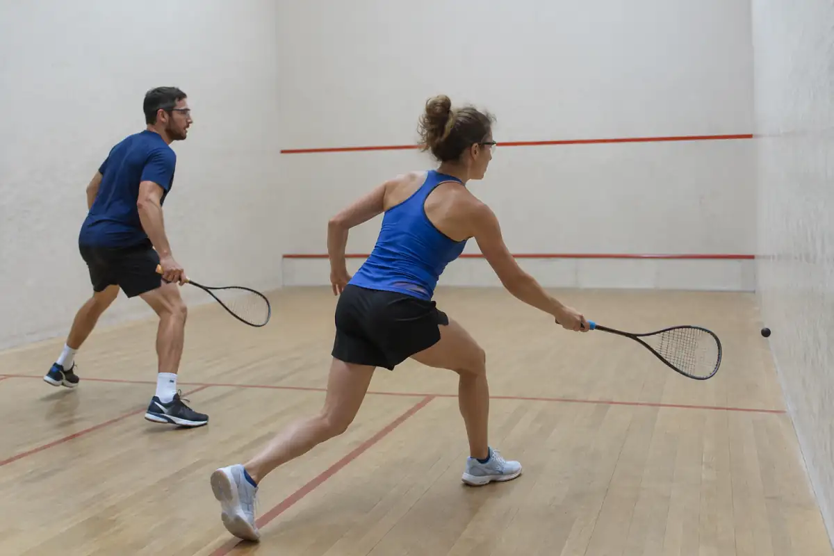 Échange de Squash 57 dans un court intérieur : un joueur frappe la balle de 57 mm vers le mur frontal.