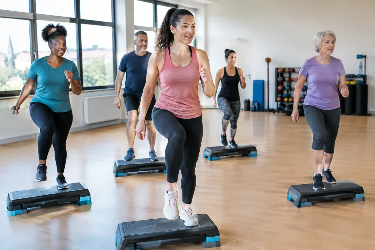 Cours de step fitness en salle : une participante monte sur sa plateforme pendant que le groupe suit la chorégraphie.
