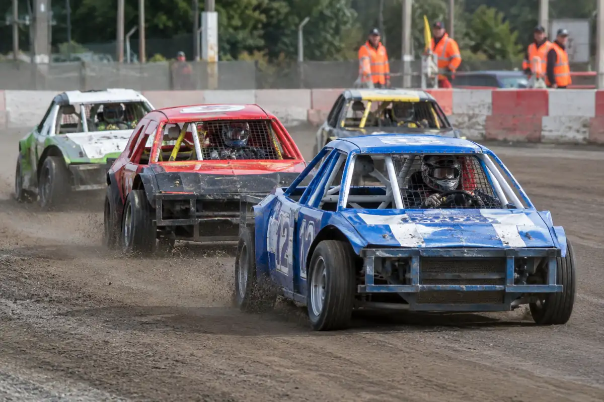 Des voitures renforcées se suivent dans un virage d’un circuit ovale lors d’une course de stock-car.