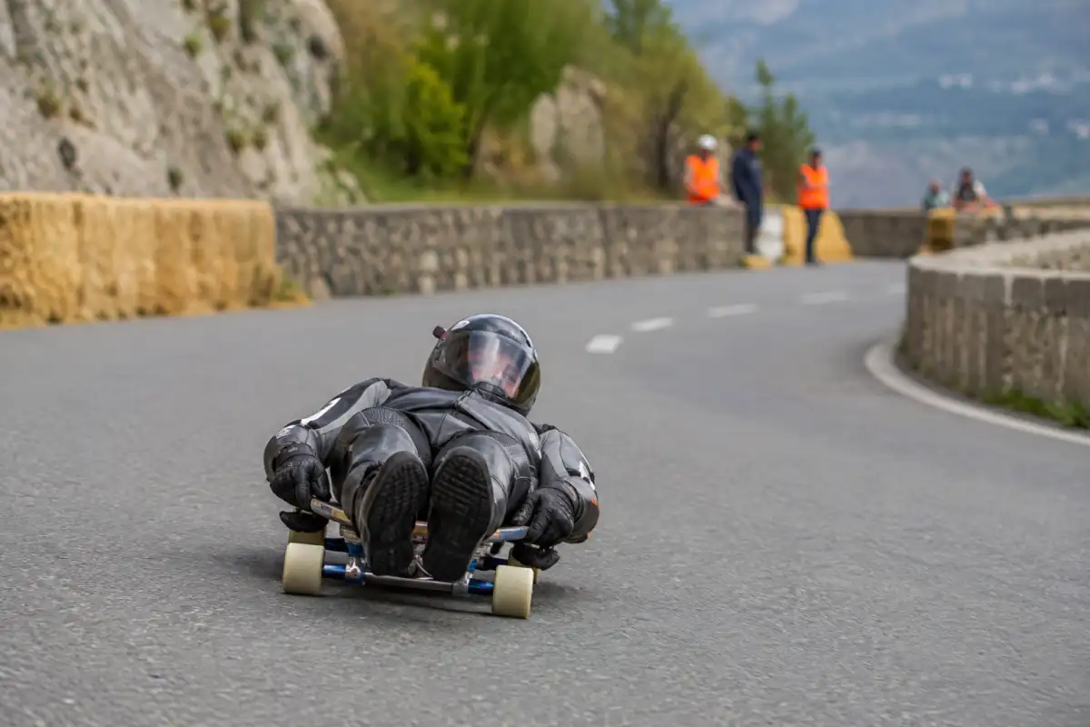 Pilote de street luge allongé sur sa planche à roulettes dans un virage d’une route fermée et sécurisée.
