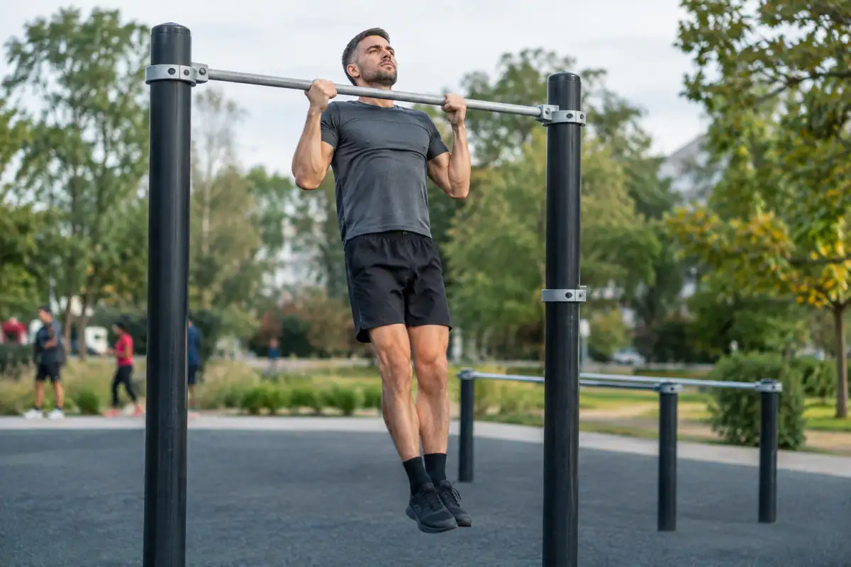 Un athlète réalise une traction contrôlée sur une barre fixe dans un parc aménagé pour le street workout.