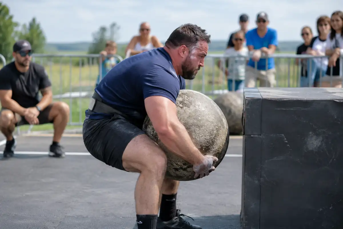 Athlète de strongman soulève une pierre atlas en béton pour la déposer sur une plateforme lors d’une compétition en extérieur.