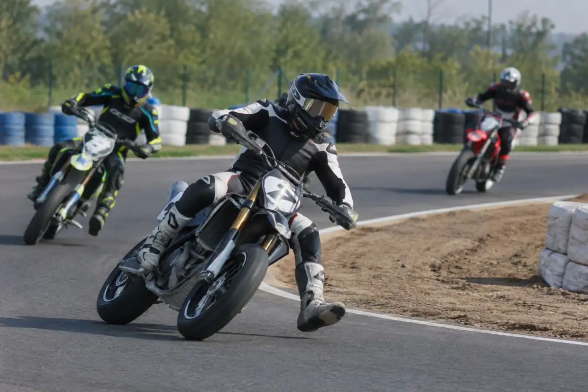 Pilotes de supermotard en virage sur un circuit mêlant asphalte et terre, équipés de casques et de combinaisons.