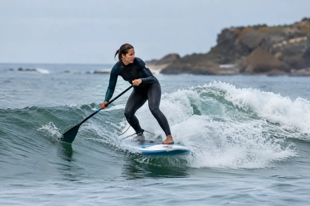 Surfeur en stand up paddle debout sur une vague, pagaie en main, sur une planche courte près d’une plage de l’Atlantique.