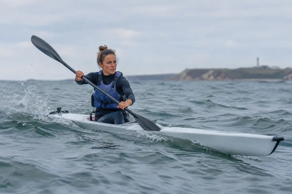 Un pagayeur en gilet de flottabilité propulse son surfski dans une petite houle au large d’une côte française.