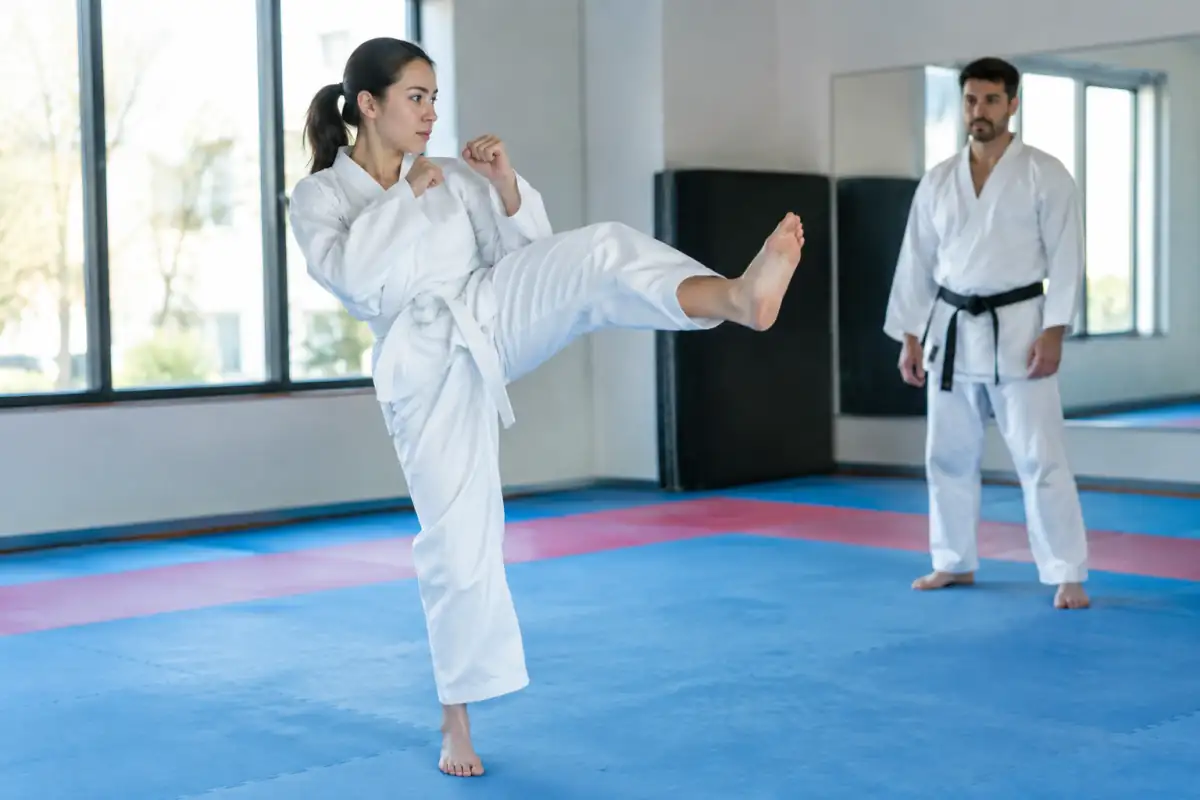 Débutant en dobok travaillant un coup de pied frontal contrôlé, genou levé et garde maintenue dans un dojang.