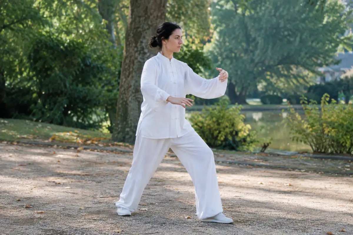 Une pratiquante exécute un pas mobile de tai-chi style Sun dans un parc, le buste droit et les bras relâchés.