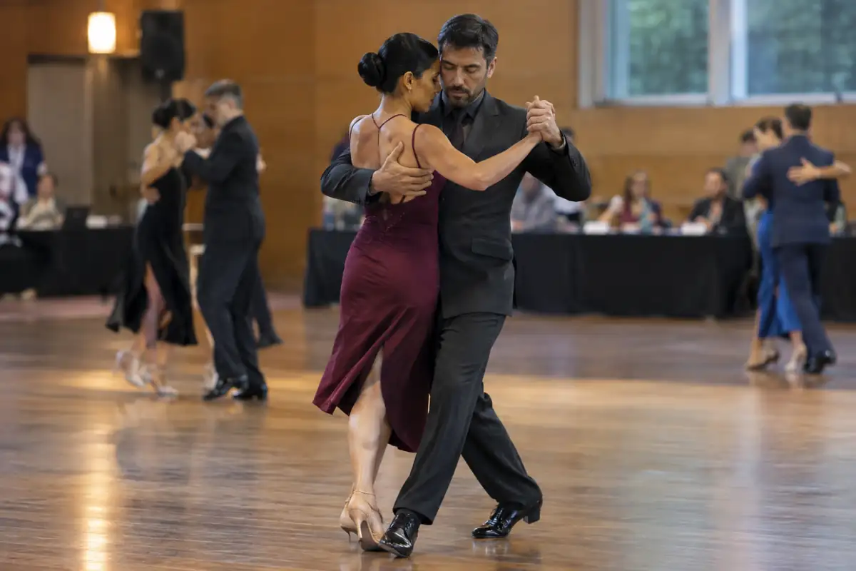 Couple de danseurs en compétition de tango argentin exécutant une marche en étreinte dans une salle de danse.