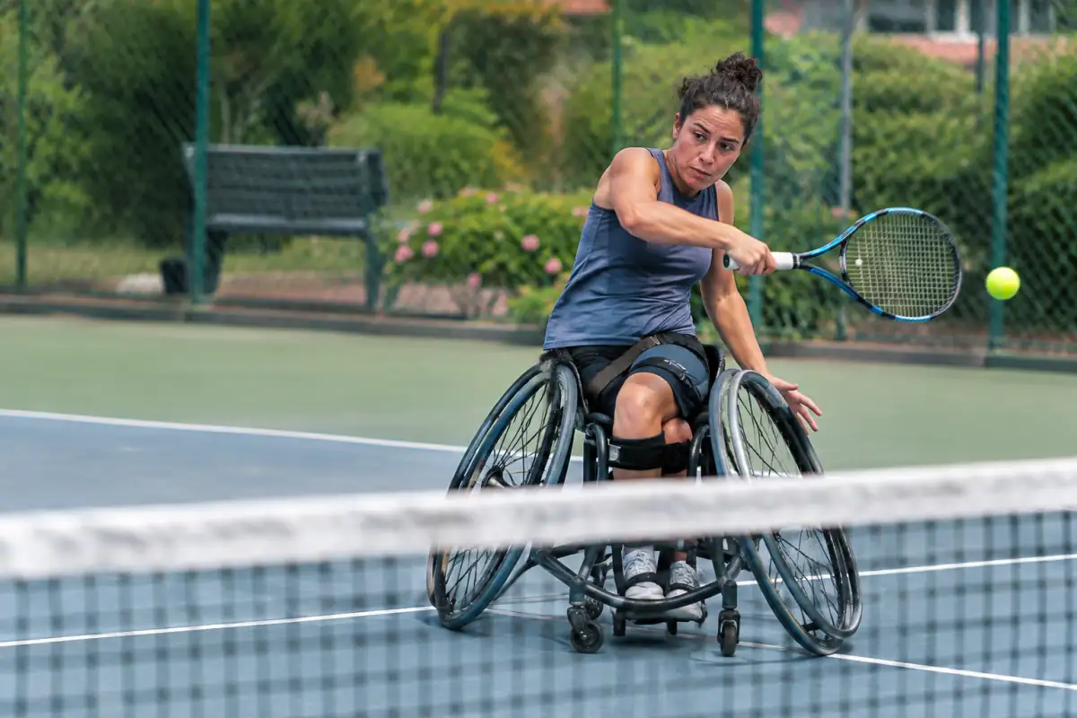 Joueuse de tennis en fauteuil roulant frappe un coup droit sur un court extérieur avec son fauteuil sportif.