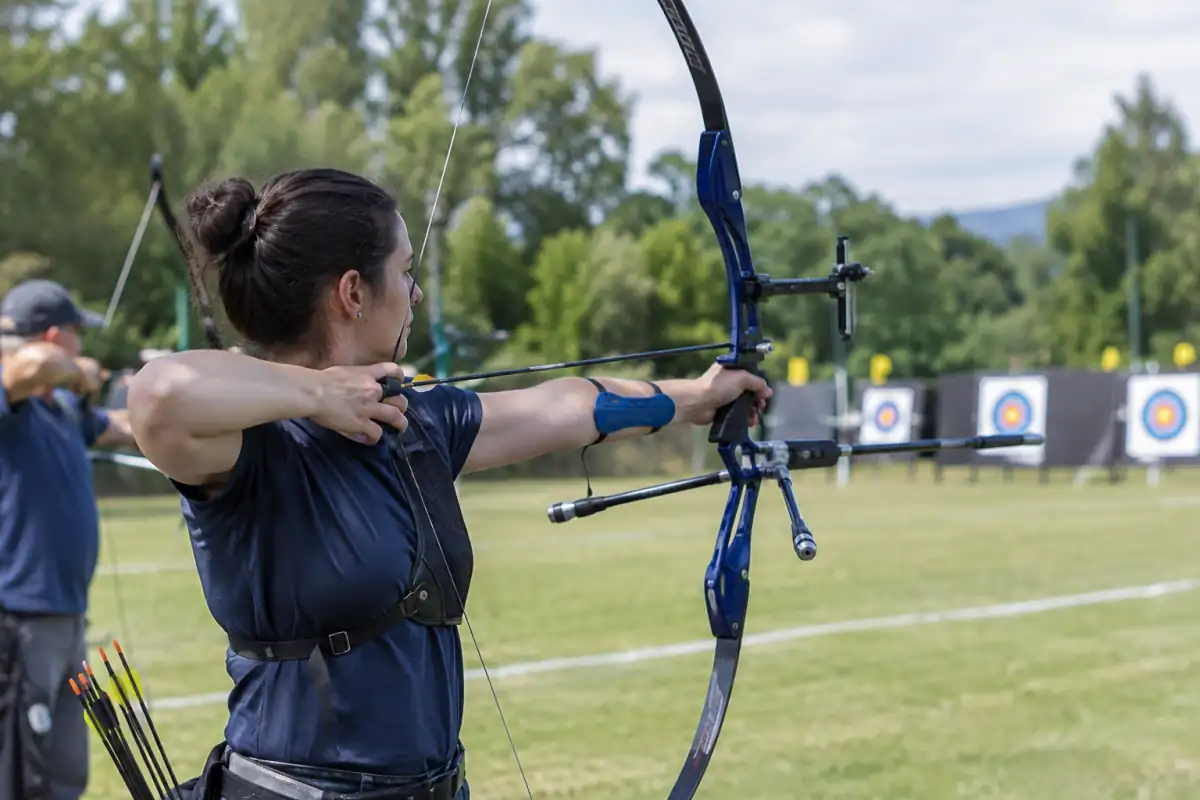 Archer en club visant une cible extérieure avec un arc classique, une flèche encochée et un protège-bras.