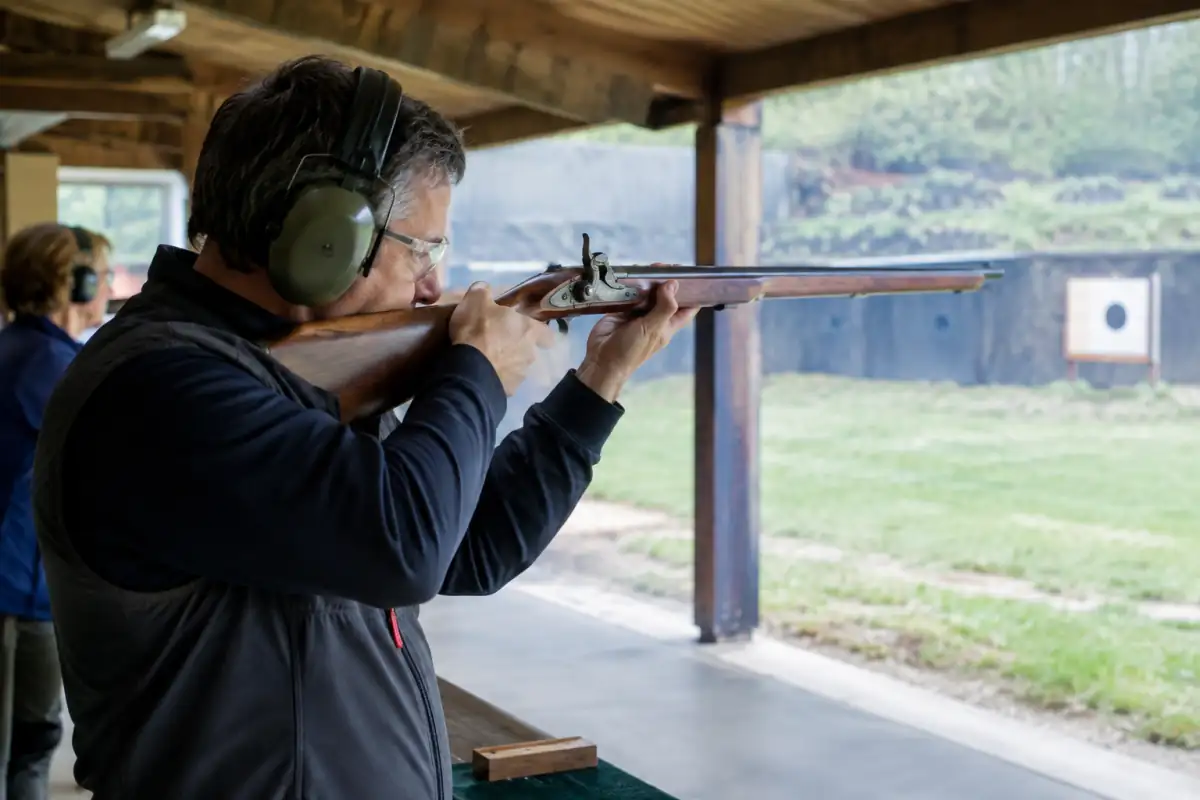 Séance de tir aux armes anciennes : un tireur protégé vise une cible avec un fusil à percussion sur un pas de tir.