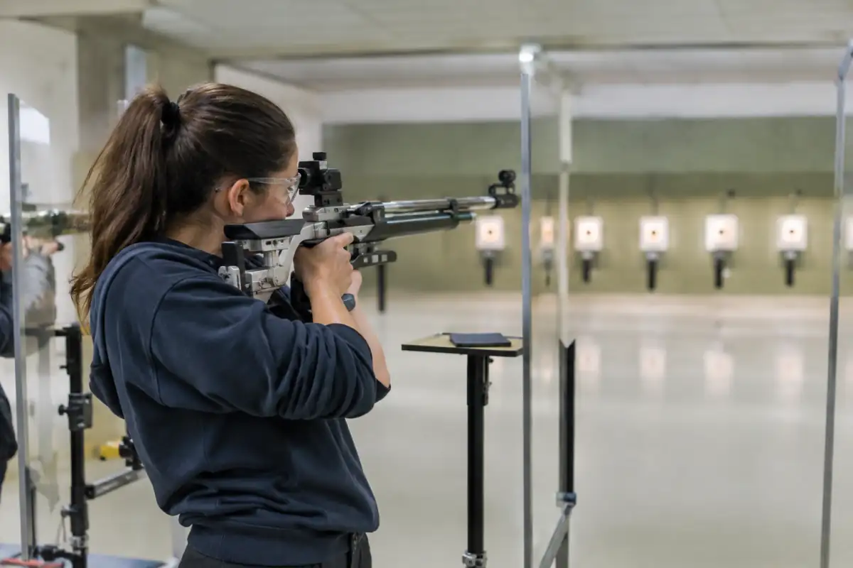 Une tireuse sportive vise une cible à 10 mètres avec une carabine à air comprimé dans un stand couvert.