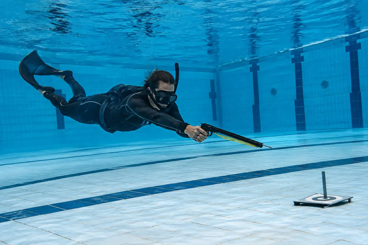 Tireur en apnée visant une cible immergée avec une arbalète lors d’une séance de tir sur cible subaquatique en piscine.
