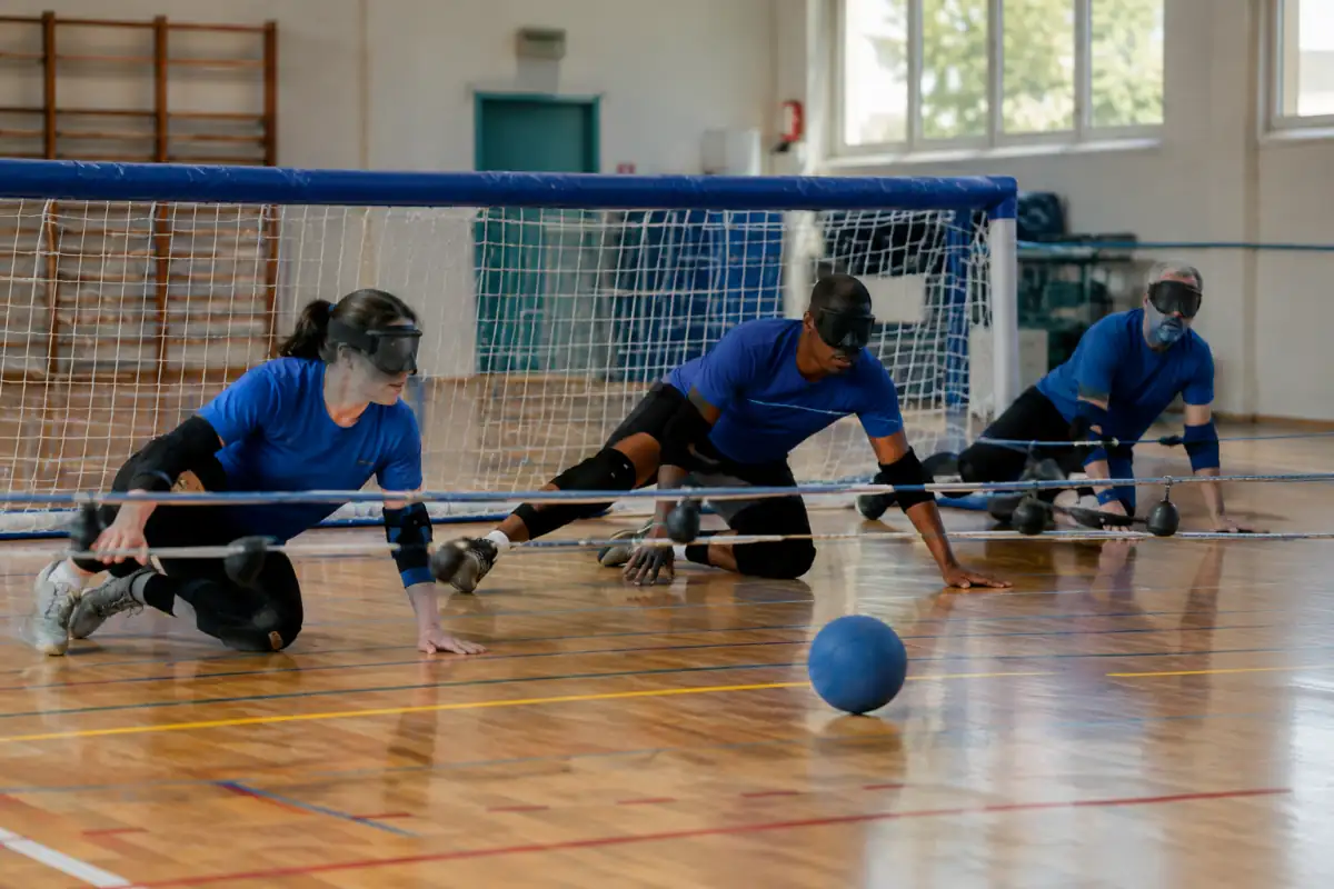 Des joueurs masqués défendent leur but au torball tandis qu’un ballon sonore roule sous les cordes dans un gymnase.