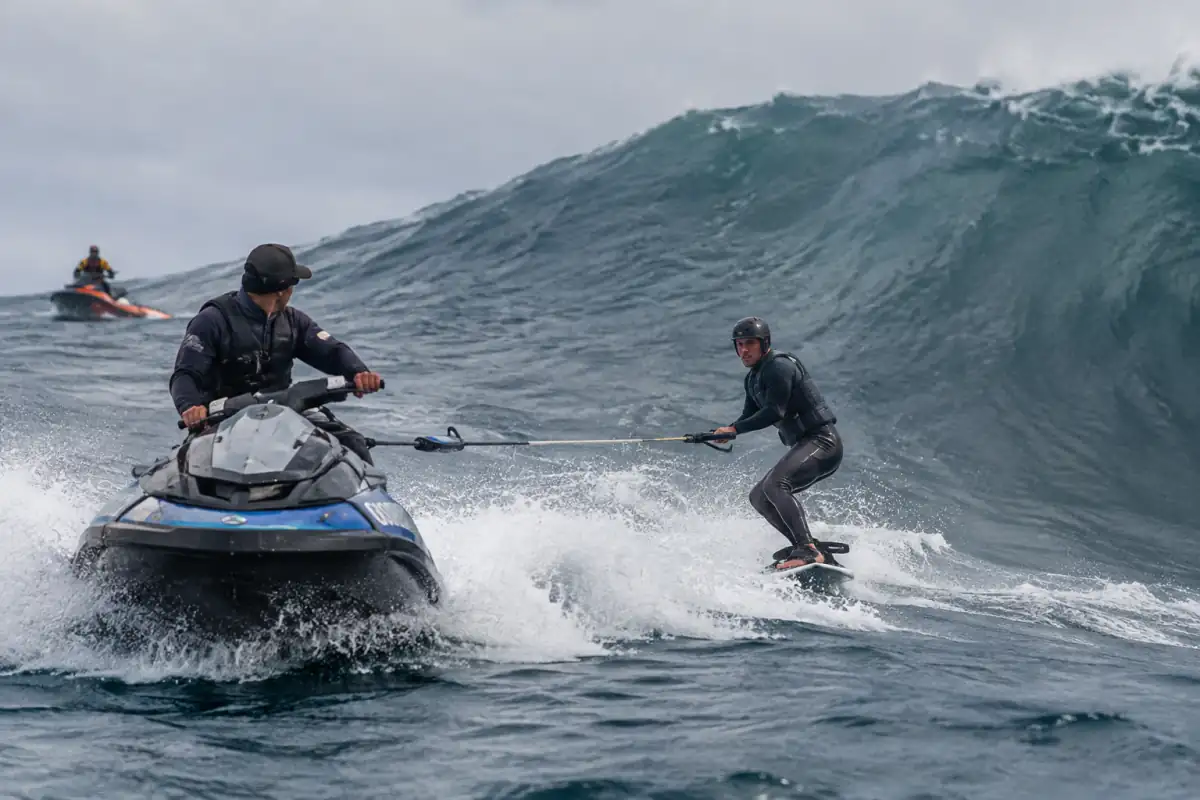 Un surfeur équipé est remorqué par un scooter des mers vers une grosse vague lors d’une séance de tow-in surfing.
