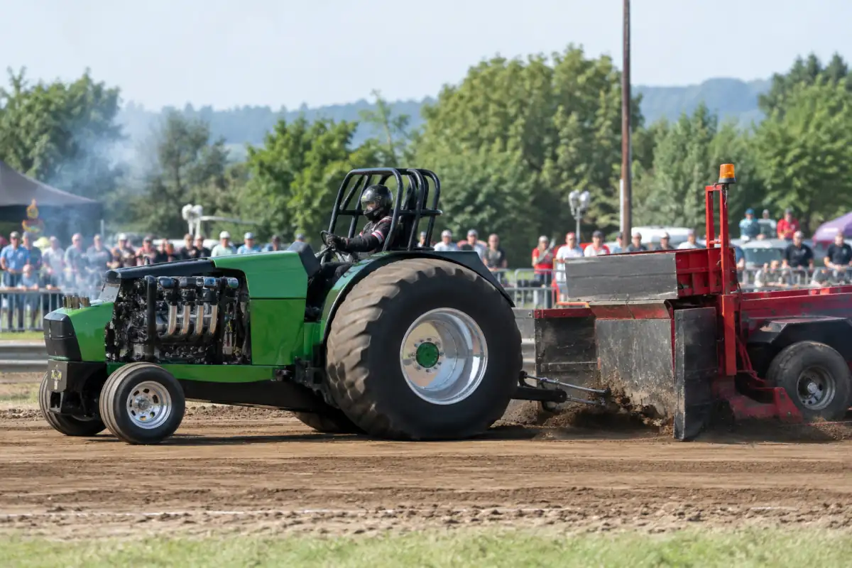 Tractor pulling : un tracteur préparé tire une remorque à poids mobile sur une piste en terre.